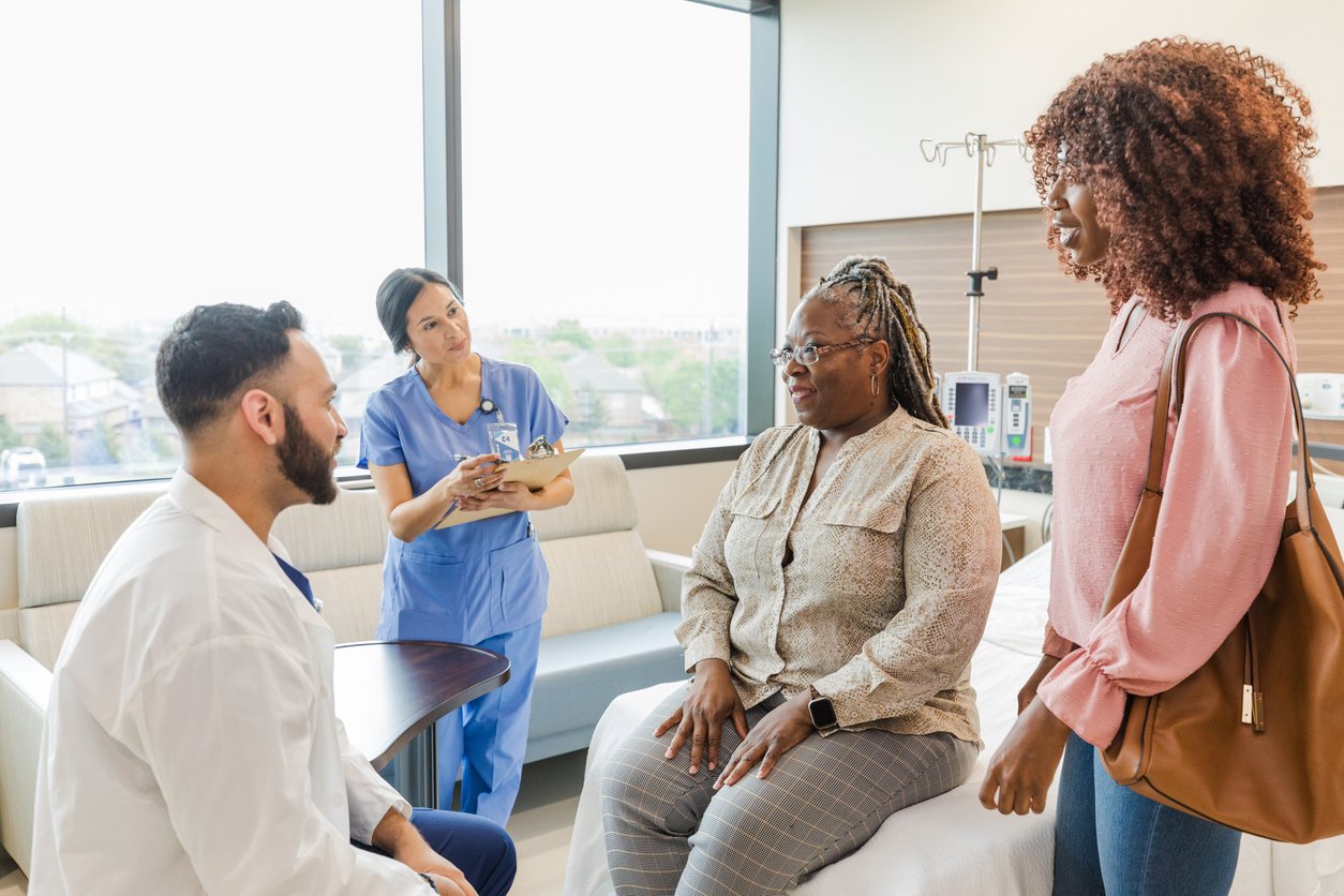 A doctor and nurse talk to a patient and caregiver in a hospital room with daughter next to her side