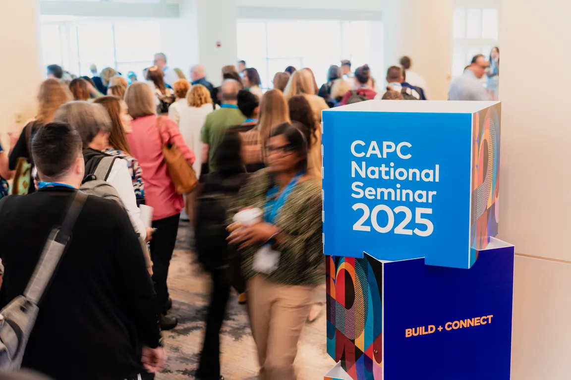 Attendees walk to their sessions next to a large sign that says CAPC National Seminar 2025