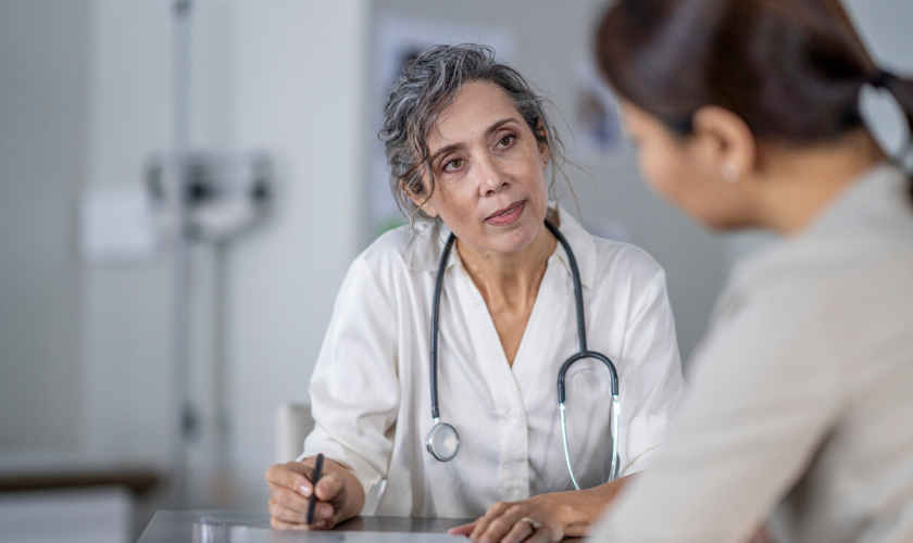 Clinician and patient talk about chronic pain management during an appointment, clinician has a stethescope around neck and is taking notes on a tablet