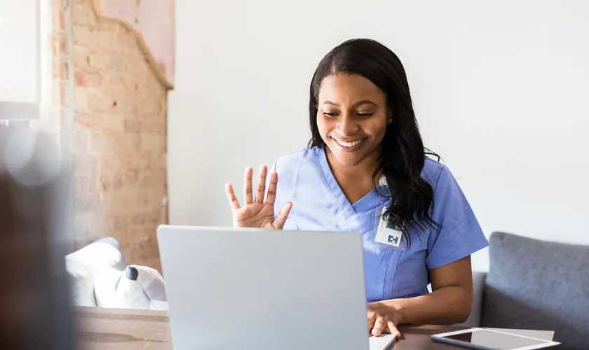 Clinician sitting in front of laptop and waving to a patient during telehealth appointment_840x500.png