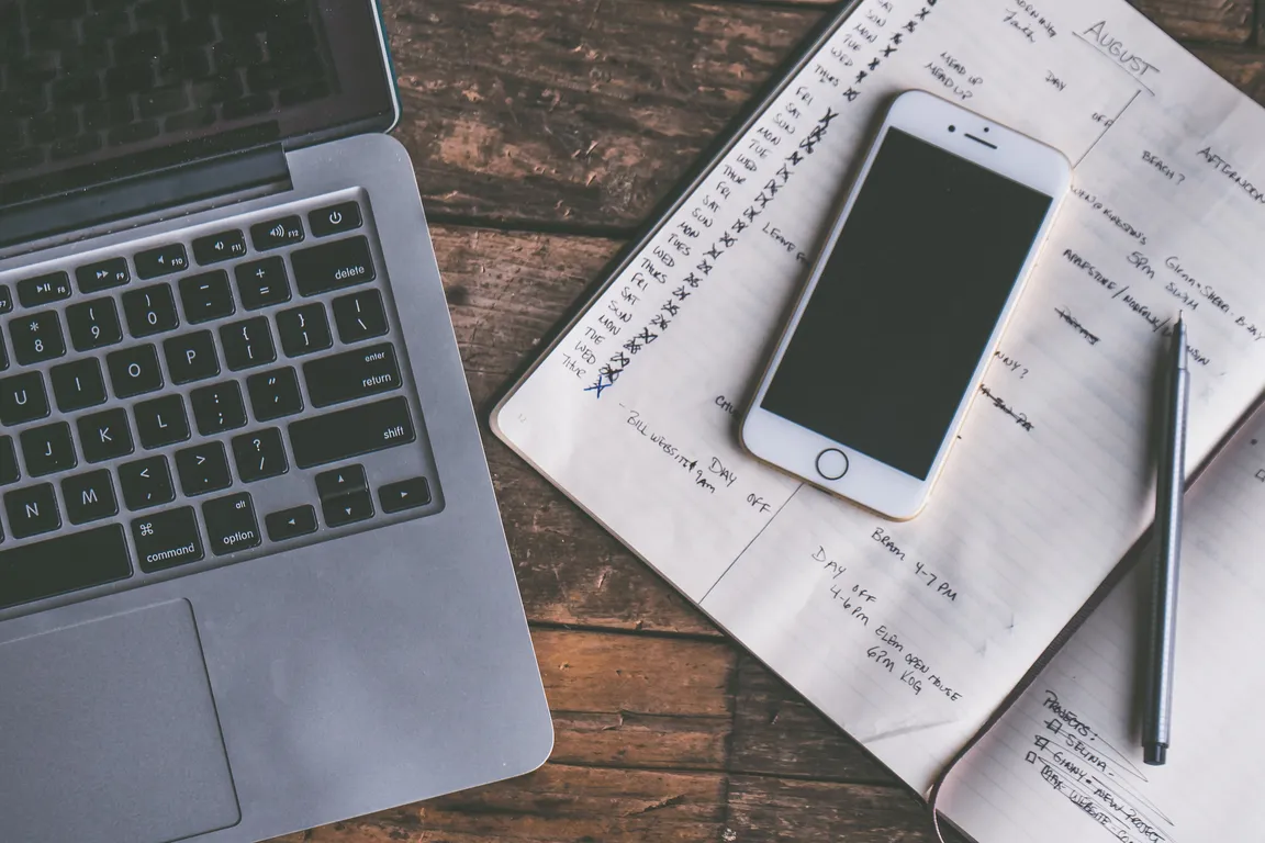 Laptop, Phone, and Calendar on Top of a Wood Desk