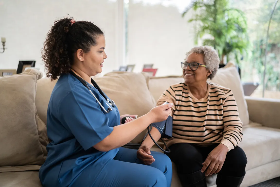 Nurse checks blood pressure of woman sitting on the couch