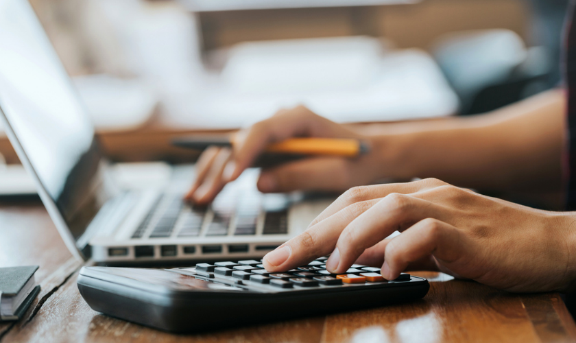 Person using calculator and typing on computer