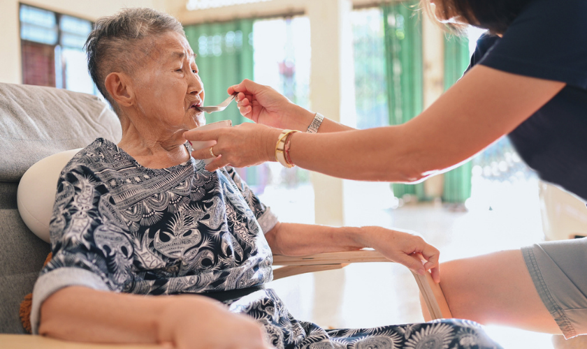 Photograph of a daughter feeding elderly mother with a spoon_840x500.png