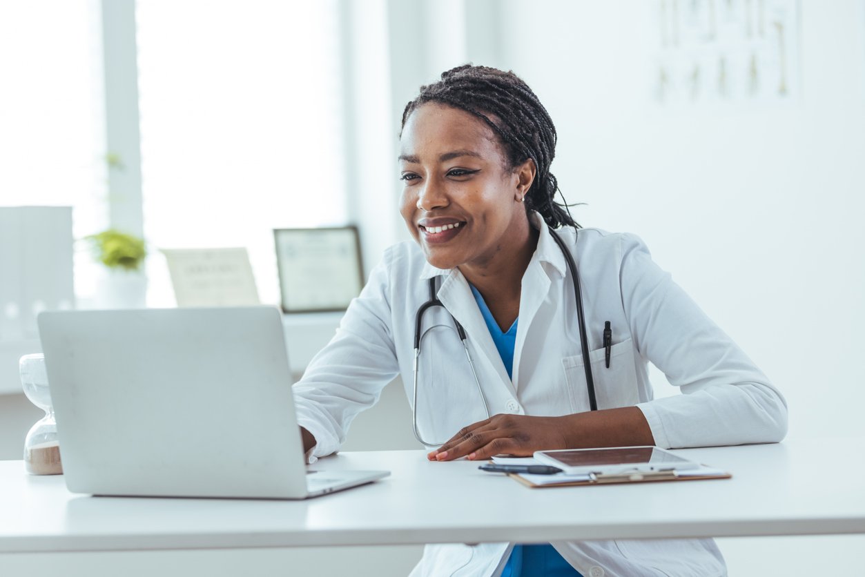 Photograph of a doctor sitting at desk while smiling at her computer