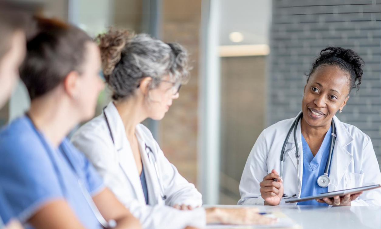 Photograph of a team of clinicians sitting at a table talking, with one clinician holding a tablet