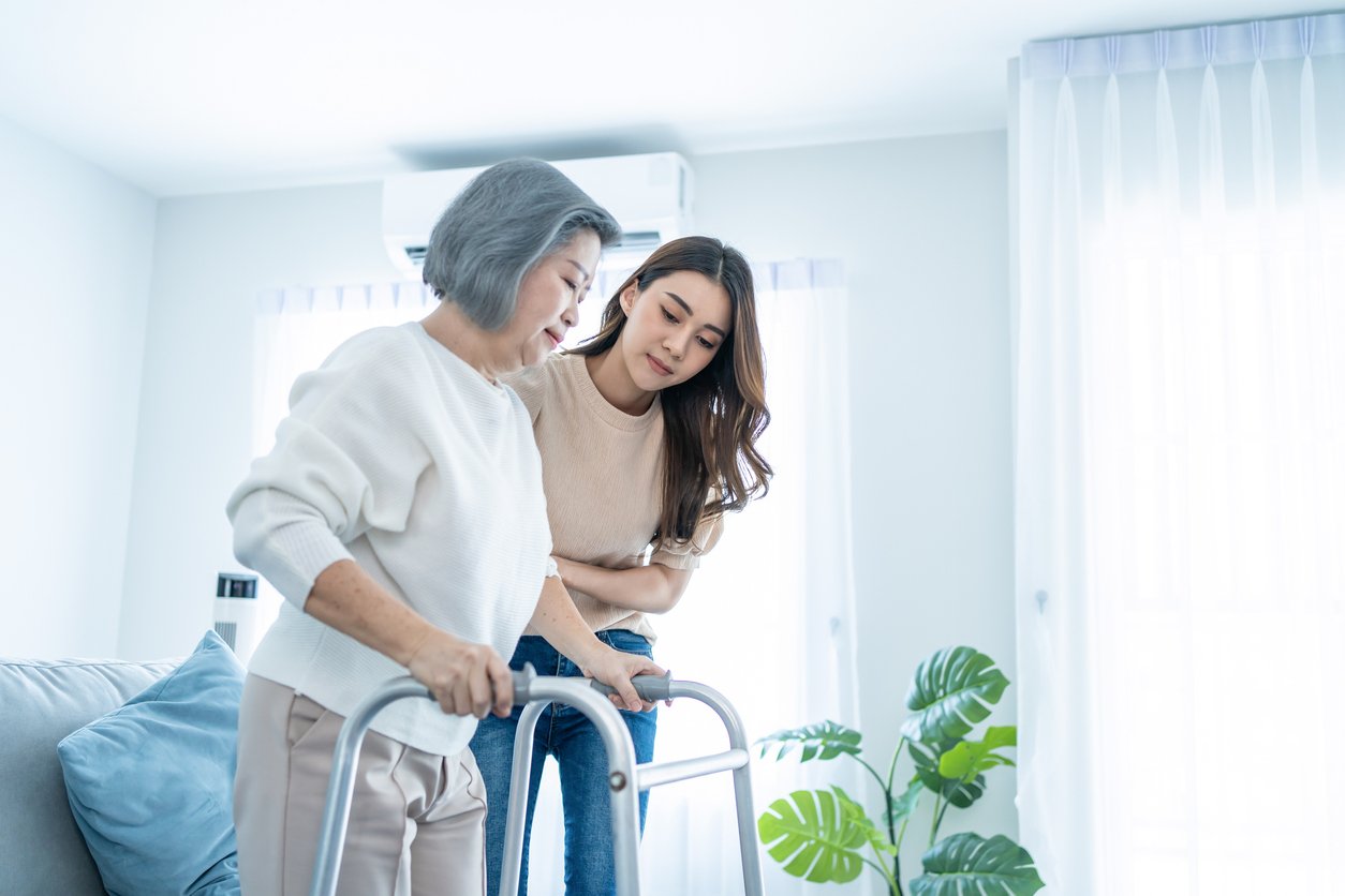 Photograph of an older woman using a walker assisted by a caregiver