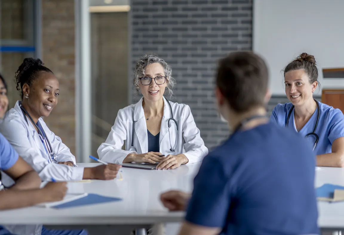 Photograph of four clinicians sitting around table looking at clinician across the table symbolizing other specialities championing palliative care