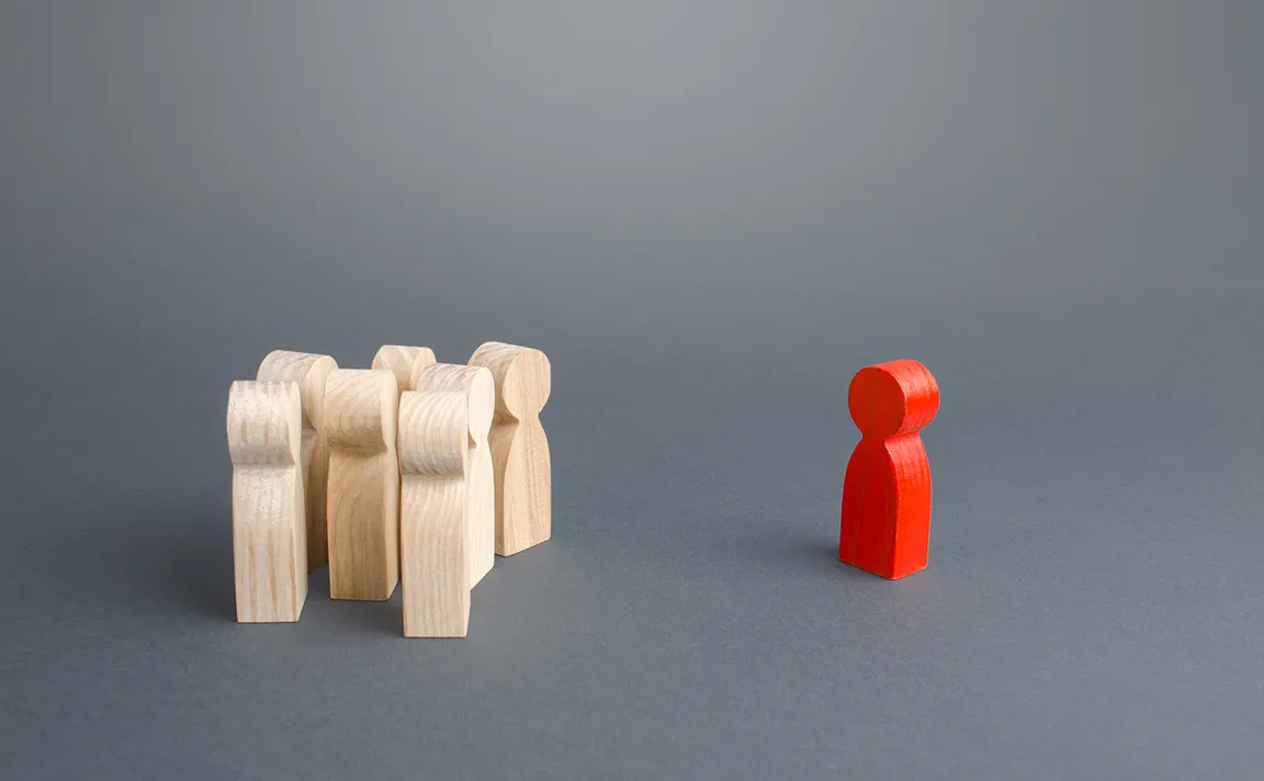 Red figurine positioned across from wooden unpainted figurines