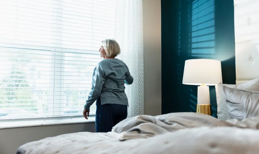 Woman opening opening up the blinds in the morning after waking up and getting out of bed_840x500
