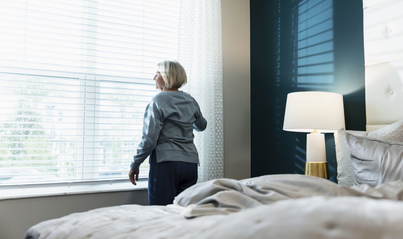 Woman opening opening up the blinds in the morning after waking up and getting out of bed