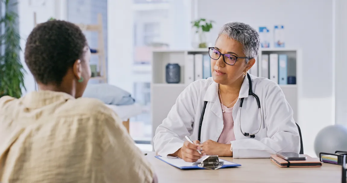Female health professional has a meeting with another female at a desk.